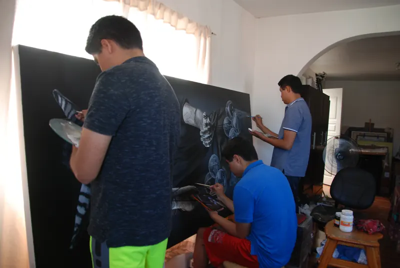 Dos de los hermanos pintan un lienzo de gran formato mientras el tercero trabaja en la tableta